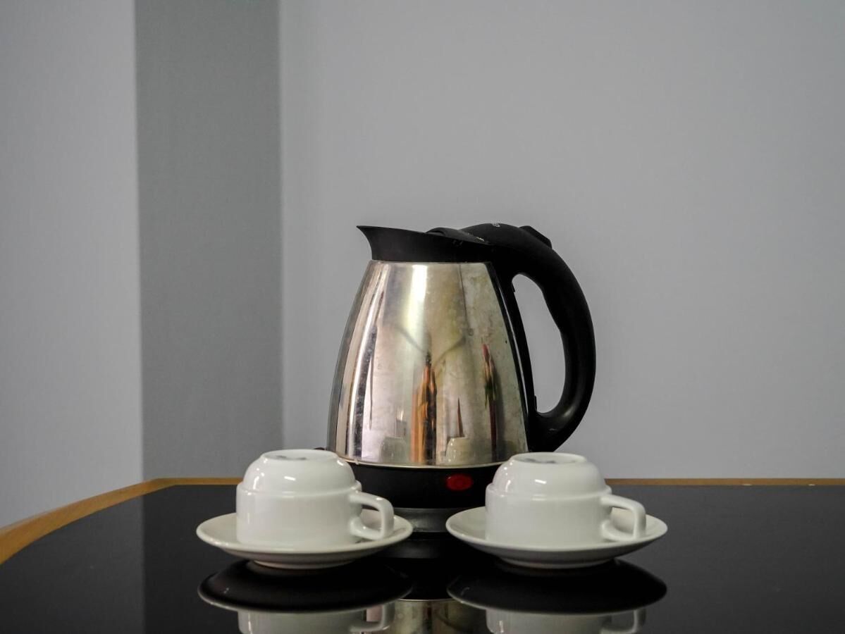 A stainless steel coffee pot with a black handle and two white cups on saucers on a reflective table.