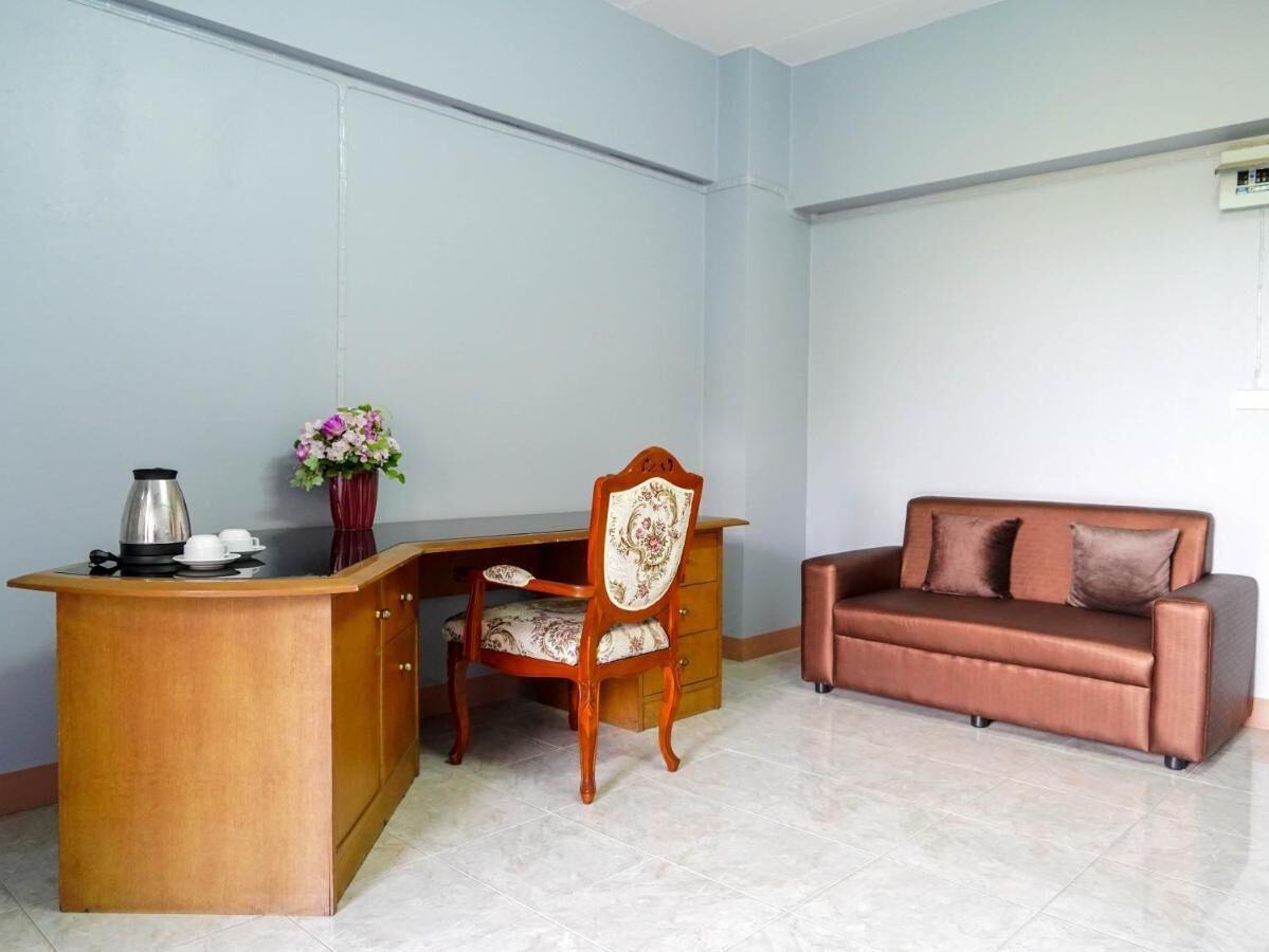 Una habitación con un escritorio de madera, una silla, un sofá marrón y un jarrón con flores.