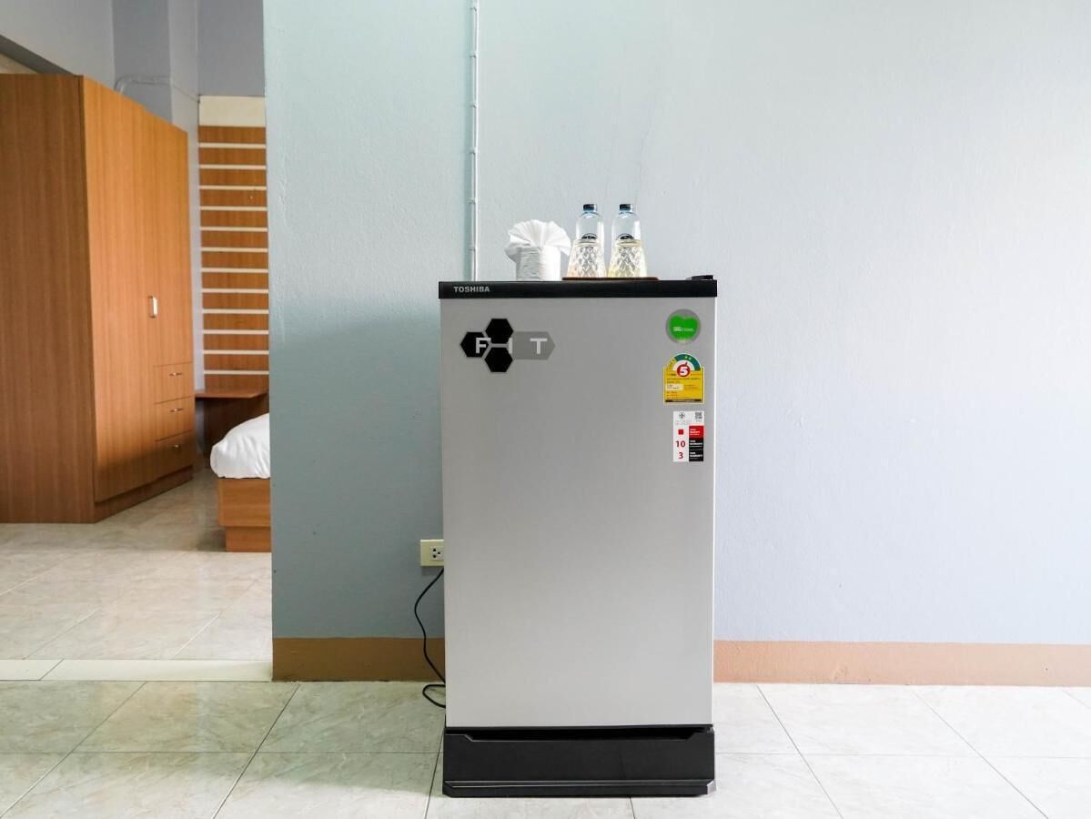 A compact refrigerator with a digital display and a water dispenser, placed in a room with a tiled floor and a wooden wardrobe.