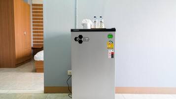 A compact refrigerator with a digital display and a water dispenser, placed in a room with a tiled floor and a wooden wardrobe.