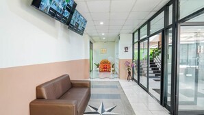 En lobby med en brun sofa, et gulv med stjerne-mønster, et vægmonteret TV og en trappe, der fører op til en etage.