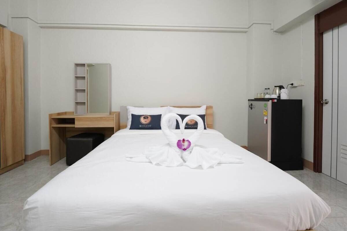 A hotel room with a neatly made bed, a wooden desk, a wardrobe, and a minibar.