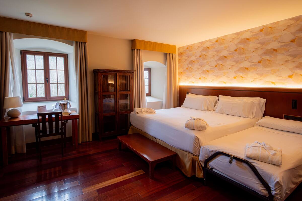 Quarto de hotel com duas camas, uma escrivaninha e um guarda-roupa.