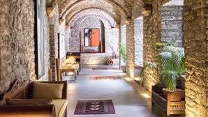 A stone-walled corridor with arches, a wooden bench, a table with a lamp, and a potted plant. - Hotel Monasterio de Boltana & SPA (Boltana)