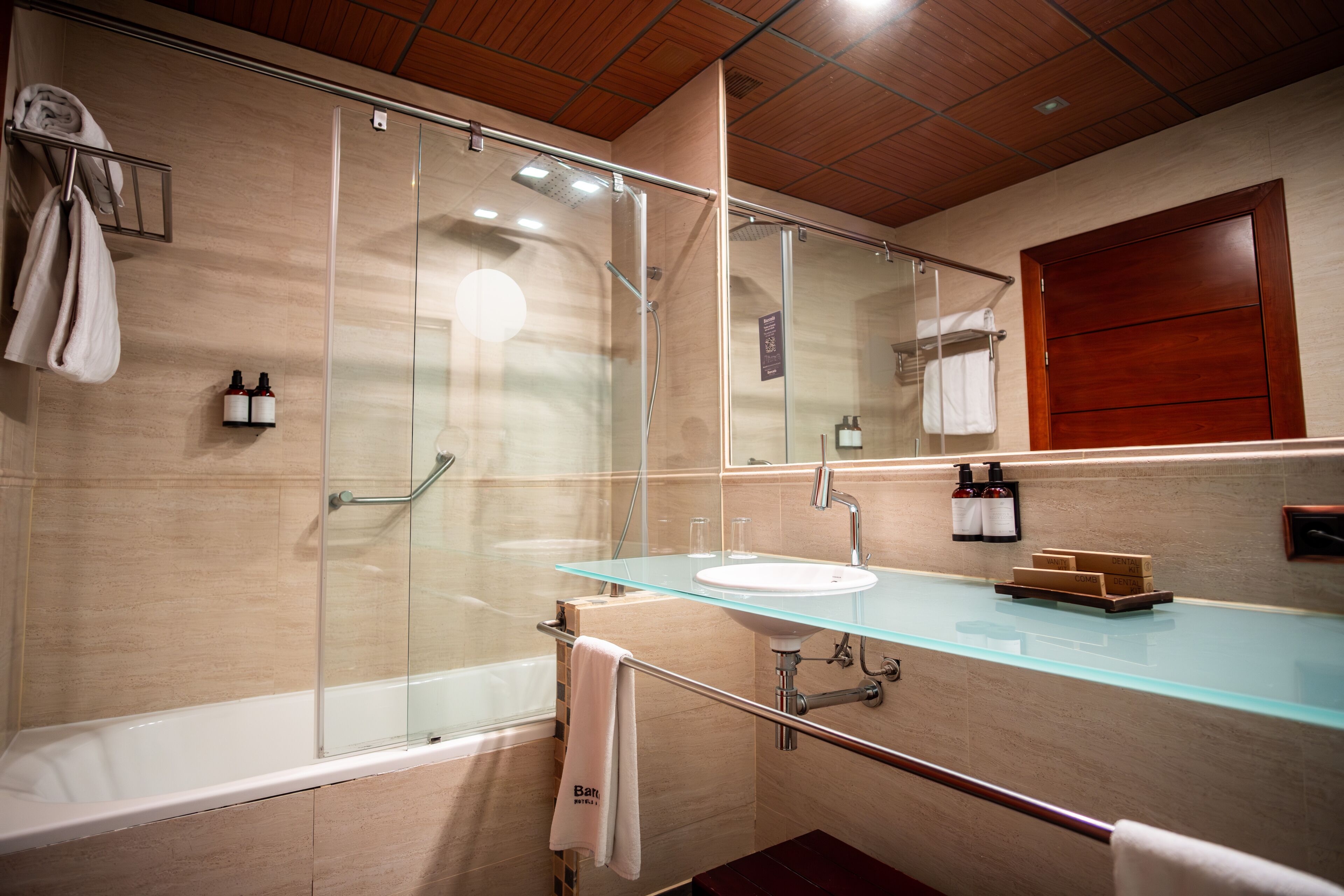 A modern bathroom with a glass shower enclosure, a glass sink, and a wooden vanity.
