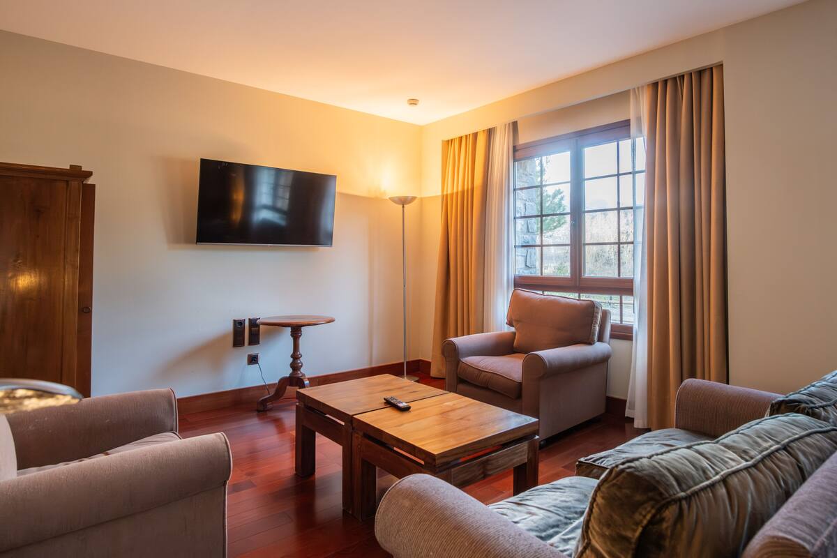 Uma sala de estar com televisão de tela plana, uma mesa de centro de madeira e dois sofás.