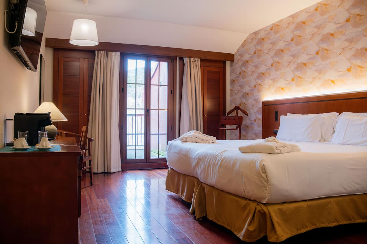 Quarto de hotel com uma cama grande, uma escrivaninha com luminária, uma cadeira e vista pela porta.