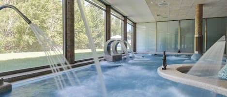 A spa area with a hot tub, a statue, and a view of trees through large windows.