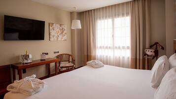 A hotel room with a large bed, a desk with a chair, a television, and a window with curtains.