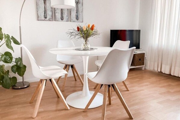 Un comedor moderno con una mesa redonda, sillas blancas y un jarrón con flores.