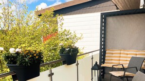 Un balcón con mobiliario exterior, plantas en macetas y vista al cielo.