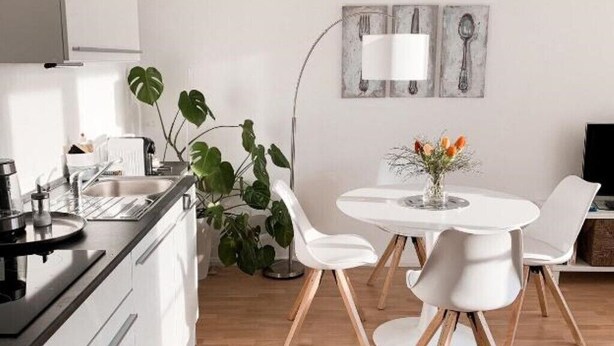 Una cocina moderna con armarios blancos, una estufa negra y una zona de comedor con una mesa y sillas blancas.