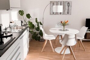 Una cocina moderna con armarios blancos, una estufa negra y una zona de comedor con una mesa y sillas blancas.