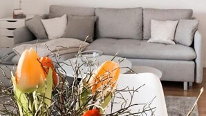 Una sala de estar moderna con un sofá gris, una mesa de centro blanca con un arreglo floral, y un cuadro en la pared.