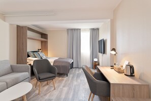 Una habitación de hotel moderna con sofá, dos sillones, escritorio, cama y televisión.