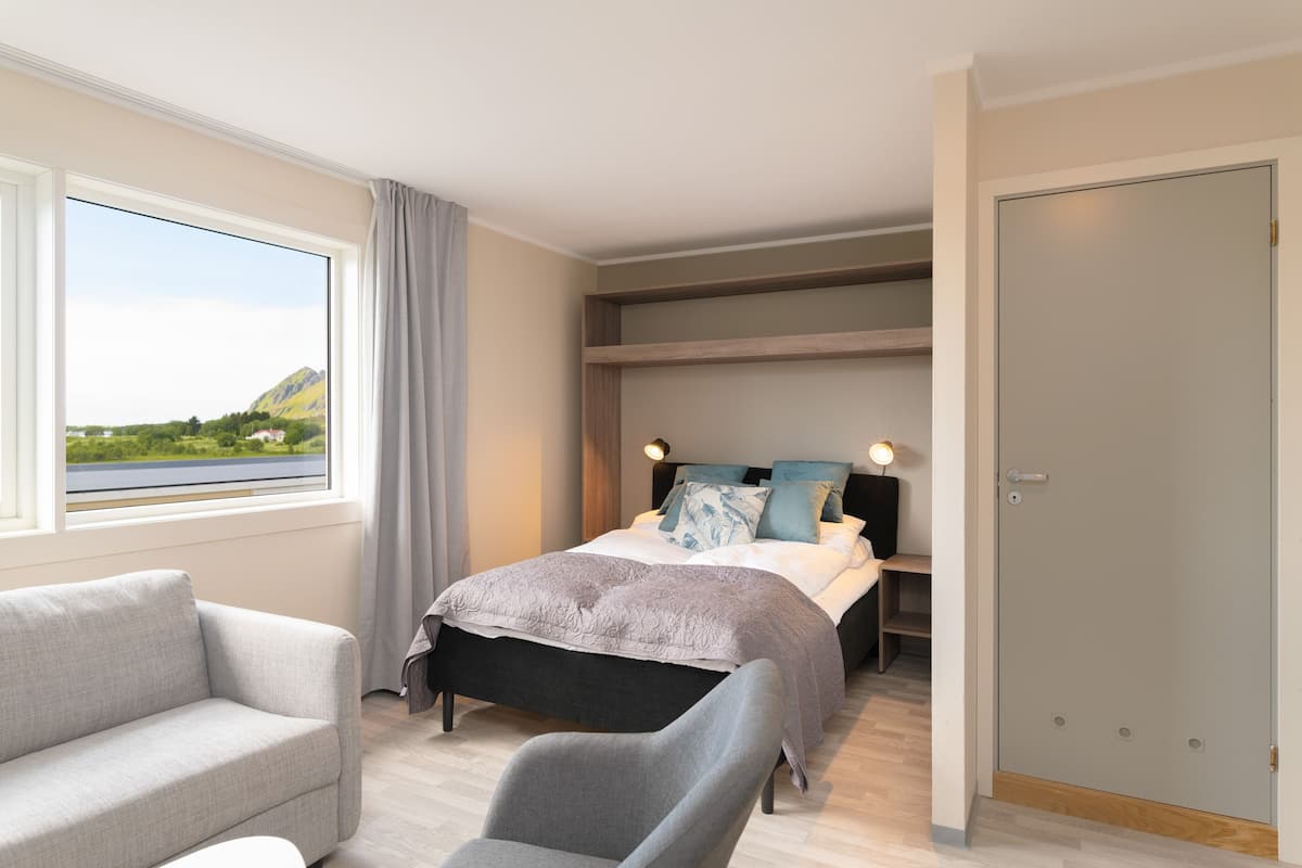 Un dormitorio con cama, sofá, escritorio y vista a un lago y montañas.