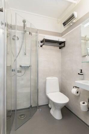 Un baño moderno con ducha de vidrio, inodoro y lavamanos con espejo.