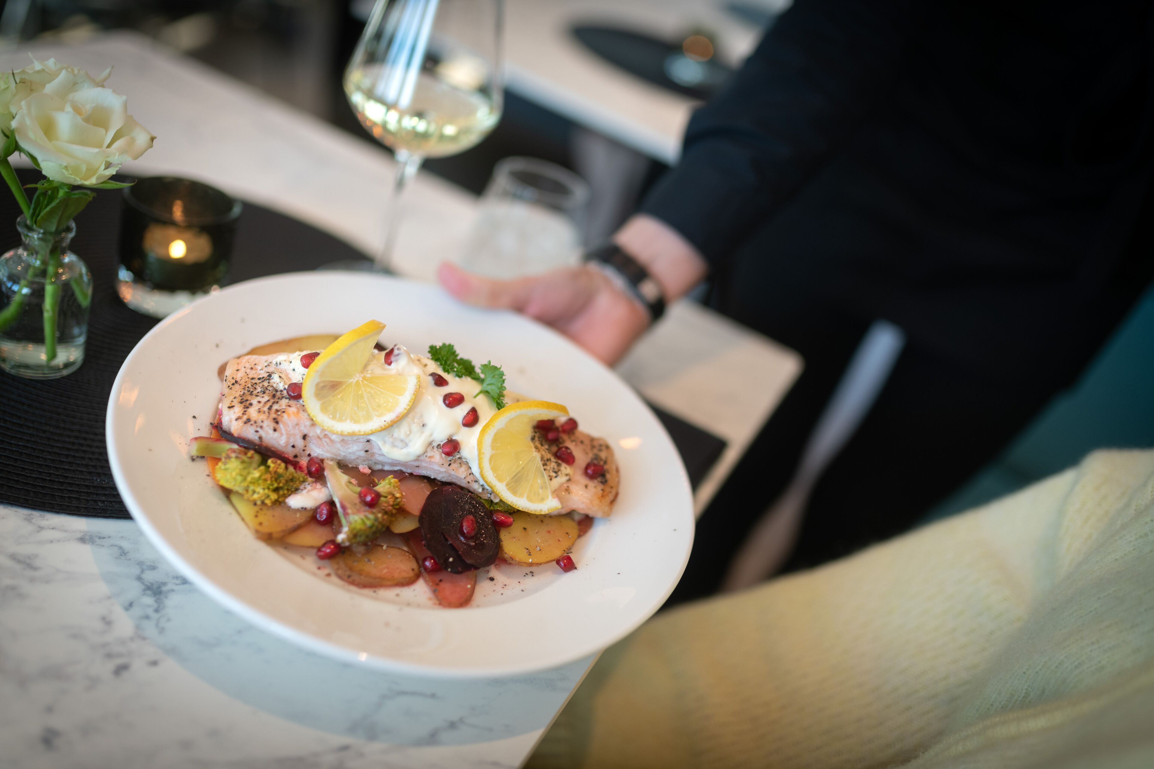 Un plato de comida con mantel blanco, una vela y una copa de vino blanco.