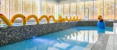 An indoor swimming pool with clear glass walls, a tiled edge, and colorful floating rings.