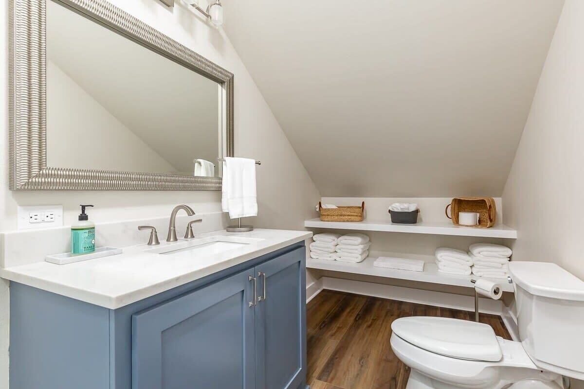 Un baño moderno con tocador blanco, espejo grande, lavamanos y retrete.