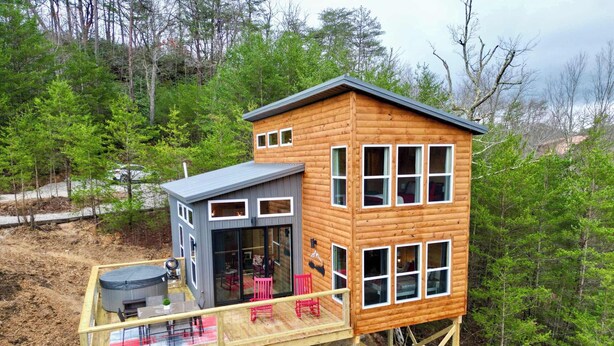 A wooden cabin with a deck, multiple windows, and a covered outdoor seating area.