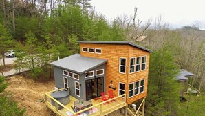 A two-story wooden cabin with a deck, a small attached garage, and a mountain view.