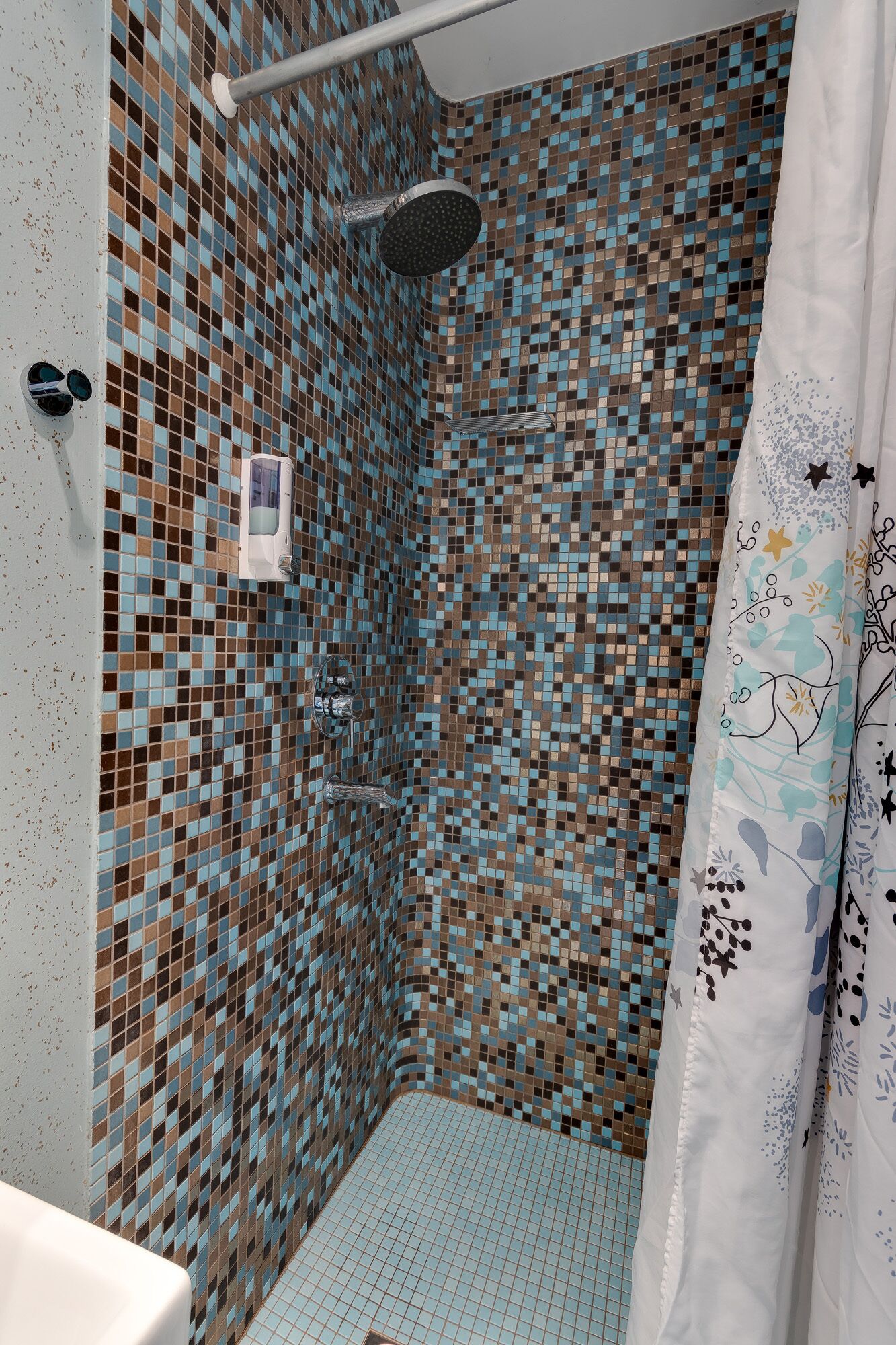 Chuveiro com paredes revestidas de mosaico e chuveiro.