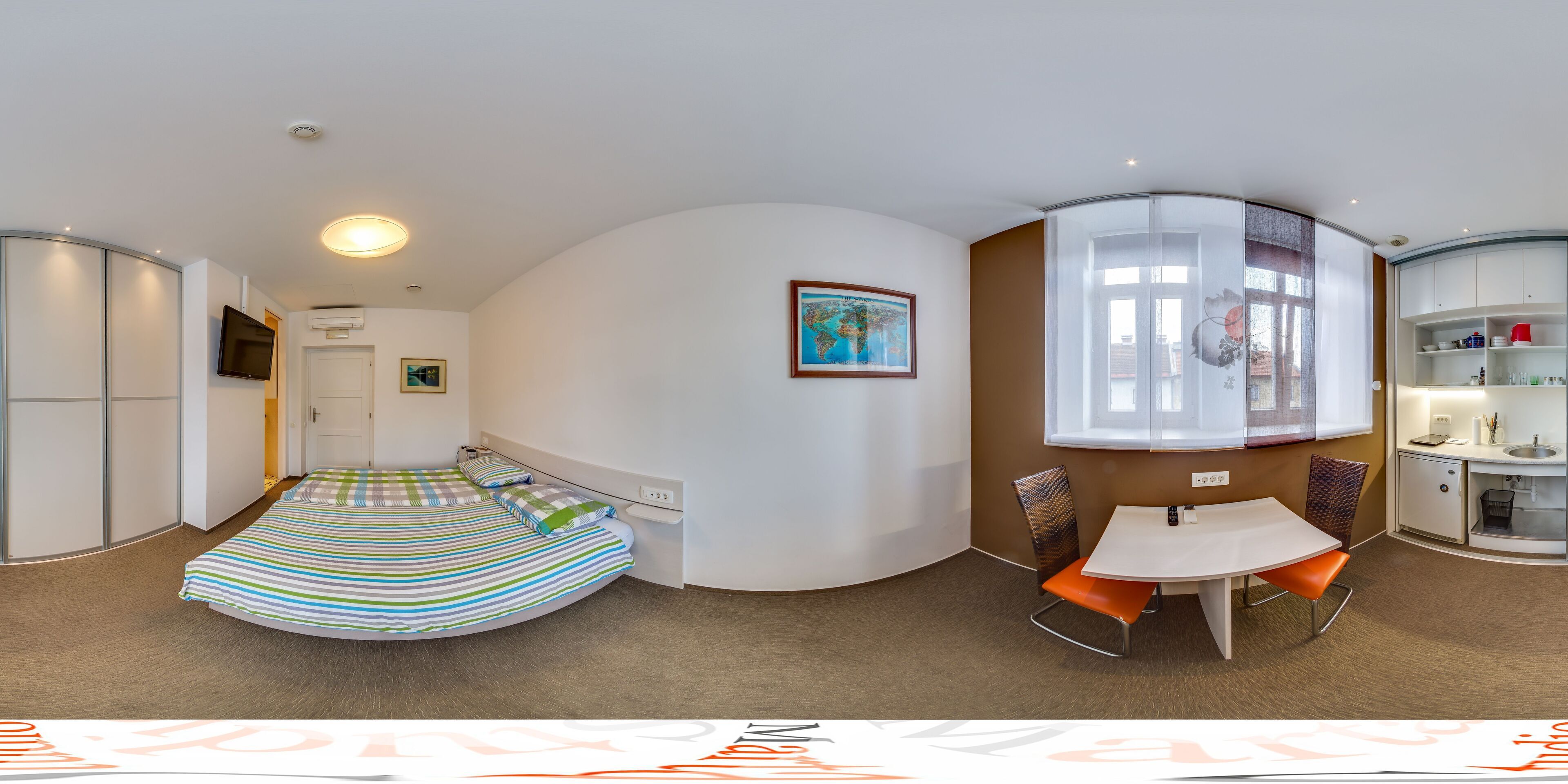 A compact hotel room with a bed, a small table with chairs, a kitchenette, and a bathroom.