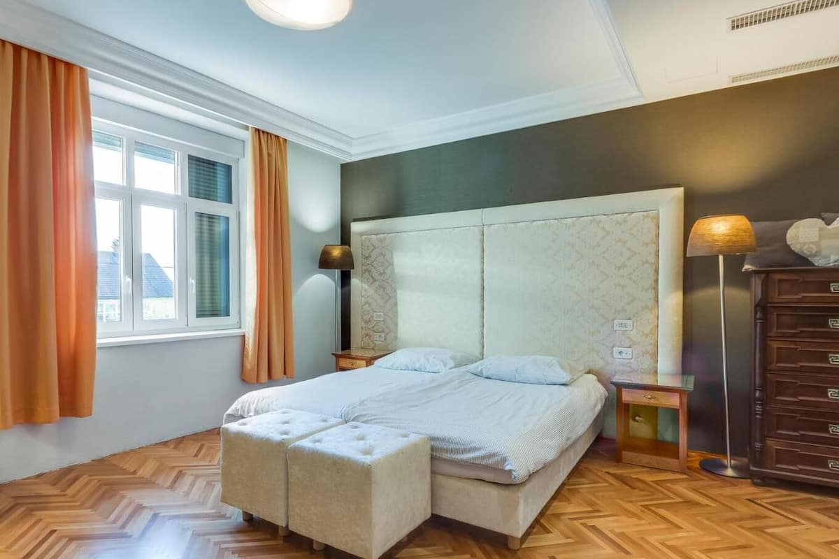 Ein Schlafzimmer mit einem großen Bett, einem Nachttisch, einer Kommode und einem Fenster mit Vorhängen.