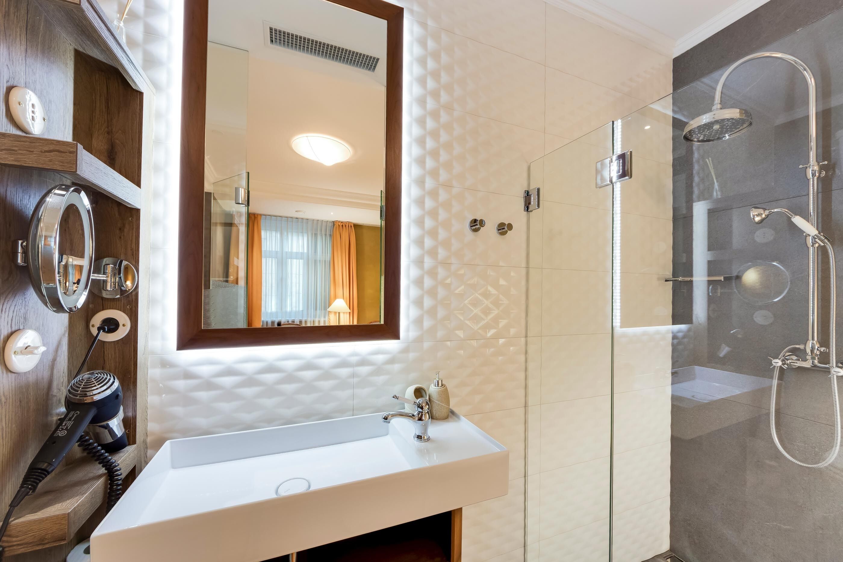 A modern bathroom with a white sink, a glass-enclosed shower, and a wooden vanity with a mirror.