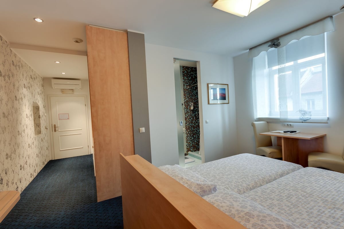 Ein Schlafzimmer mit Bett, Schreibtisch, Stuhl, Fenster und Tür.