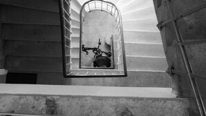 Un escalier en colimaçon avec une rampe en métal, menant à un petit espace clos où se trouvent un vélo et un casque.