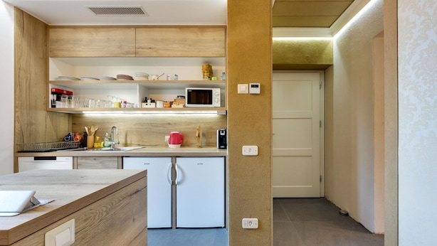 Une cuisine moderne avec des meubles en bois, un four à micro-ondes et un réfrigérateur. On y trouve des étagères remplies d’assiettes et un évier avec des ustensiles.