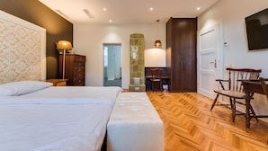 Une chambre d’hôtel avec un grand lit, un plancher en bois, un bureau avec une chaise et un téléviseur fixé au mur.