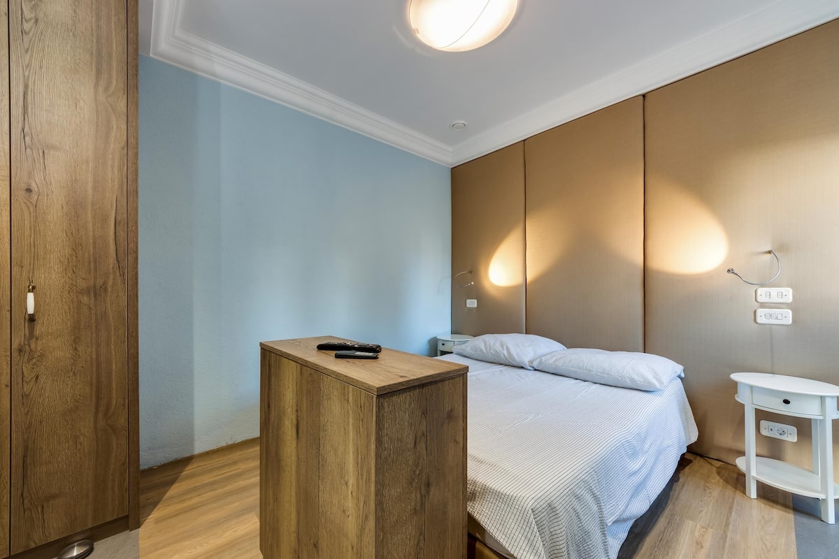 Ein Schlafzimmer mit Bett, Holzschrank, Nachttisch und Wandleuchte.