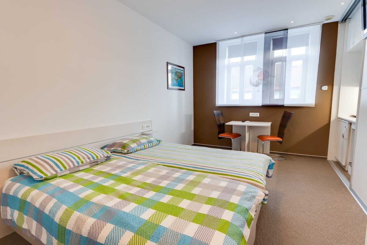 Ein Schlafzimmer mit einem Bett, einem Schreibtisch, zwei Stühlen und einem Fenster.
