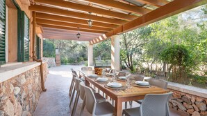 Un patio exterior con mesa de madera dispuesta para comer, rodeado de muros de piedra y contraventanas verdes.