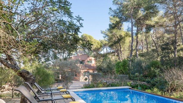 Zona junto a la piscina con sillones de descanso y vista despejada a una casa al fondo.