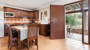 Una cocina con armarios de madera, una mesa de comedor con sillas y un ventanal corredizo que da a un espacio exterior.