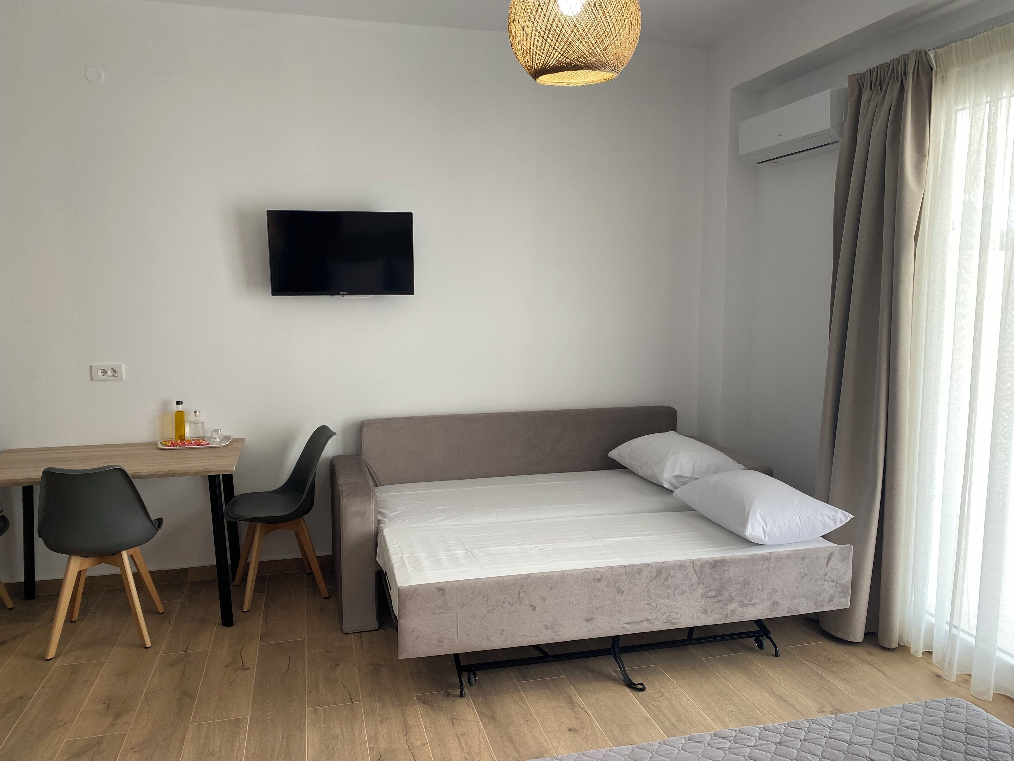 Una habitación moderna con cama, escritorio, silla, televisor y ventana con cortinas.