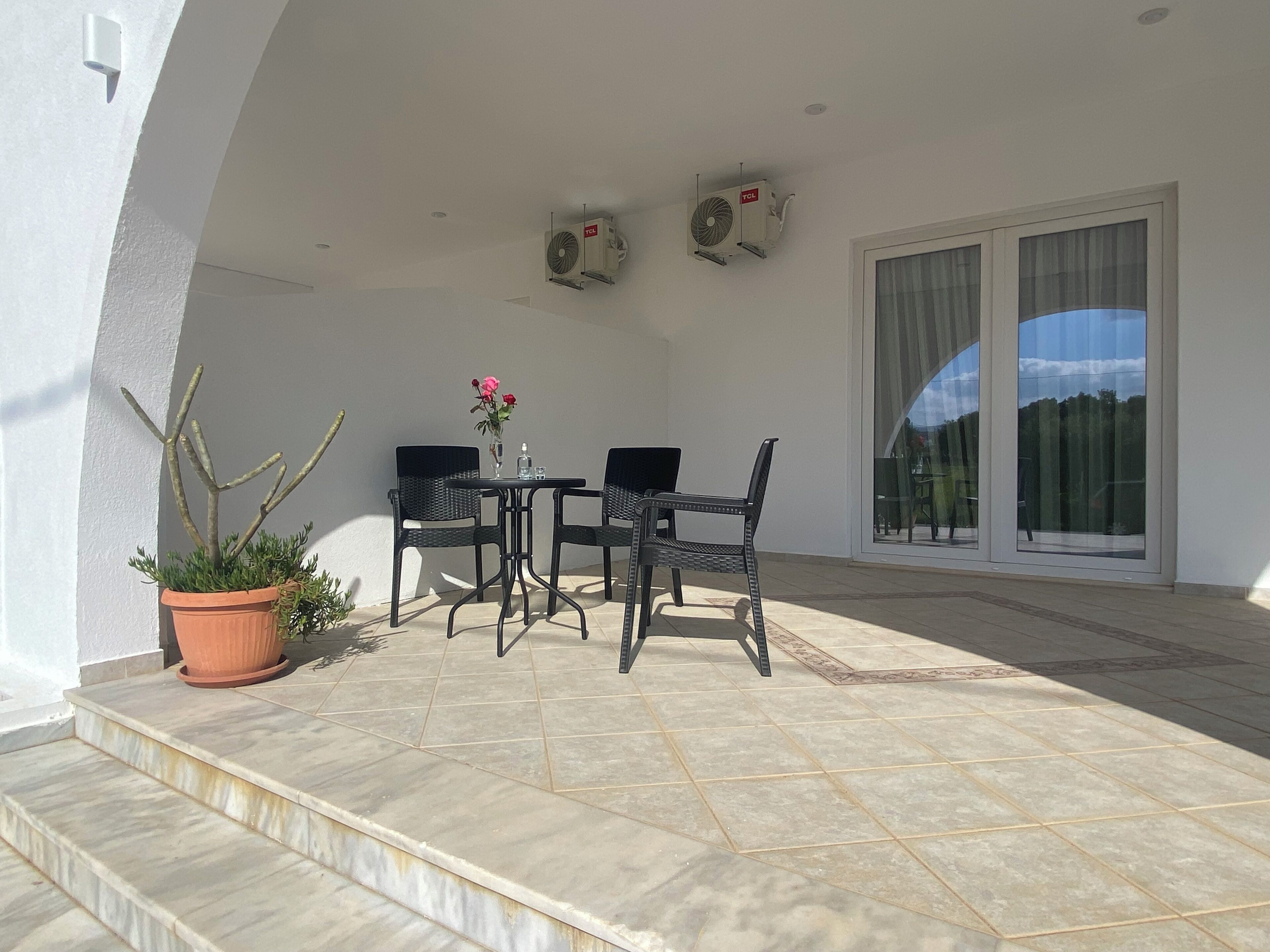 A patio with a table and chairs, a potted plant, and a sliding glass door.