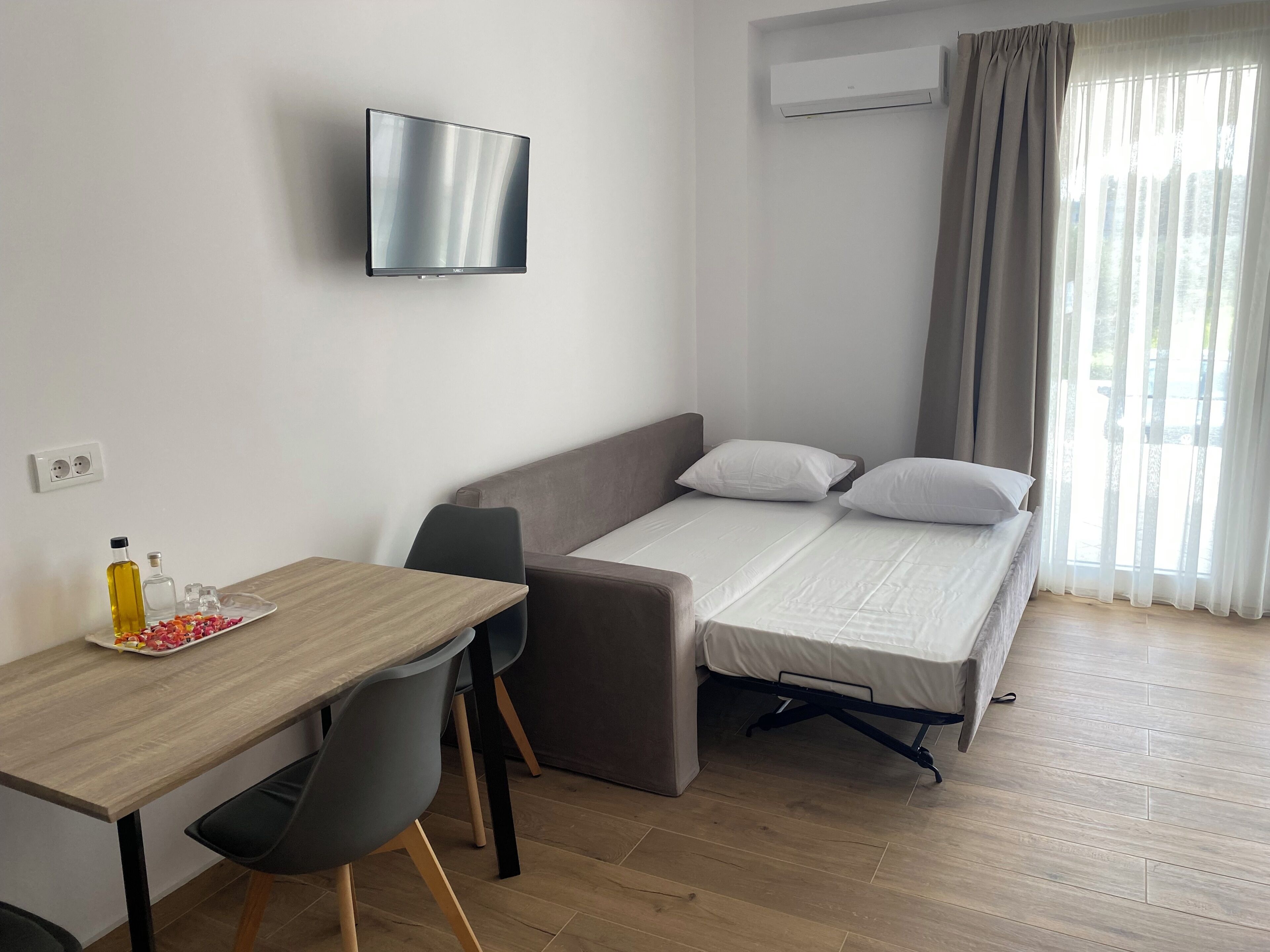 A compact room with a bed, a desk, a chair, a TV, and an air conditioning unit.