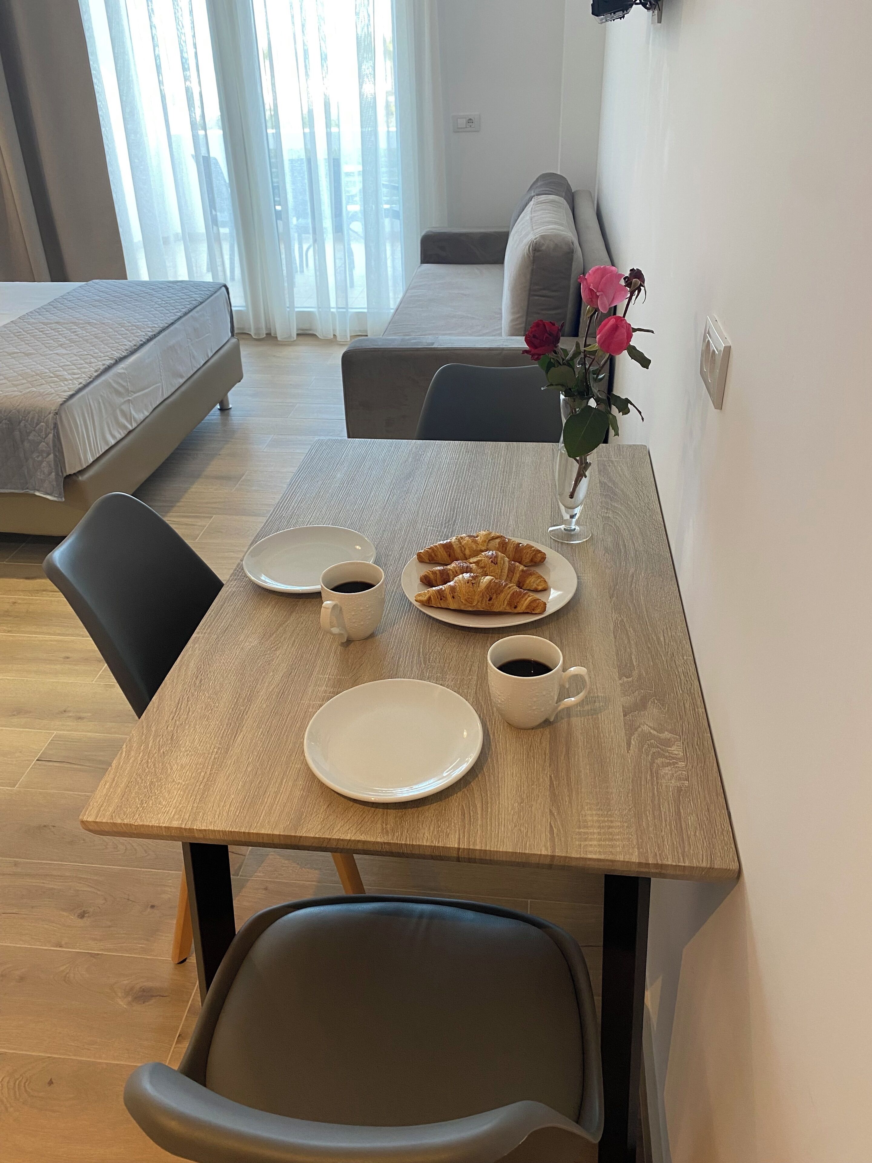 A dining area with a table set for two, a bed, a sofa, and a vase with flowers.