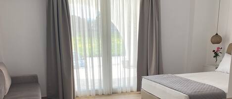 Una habitación de hotel moderna con cama, escritorio, silla y un ventanal con cortinas.