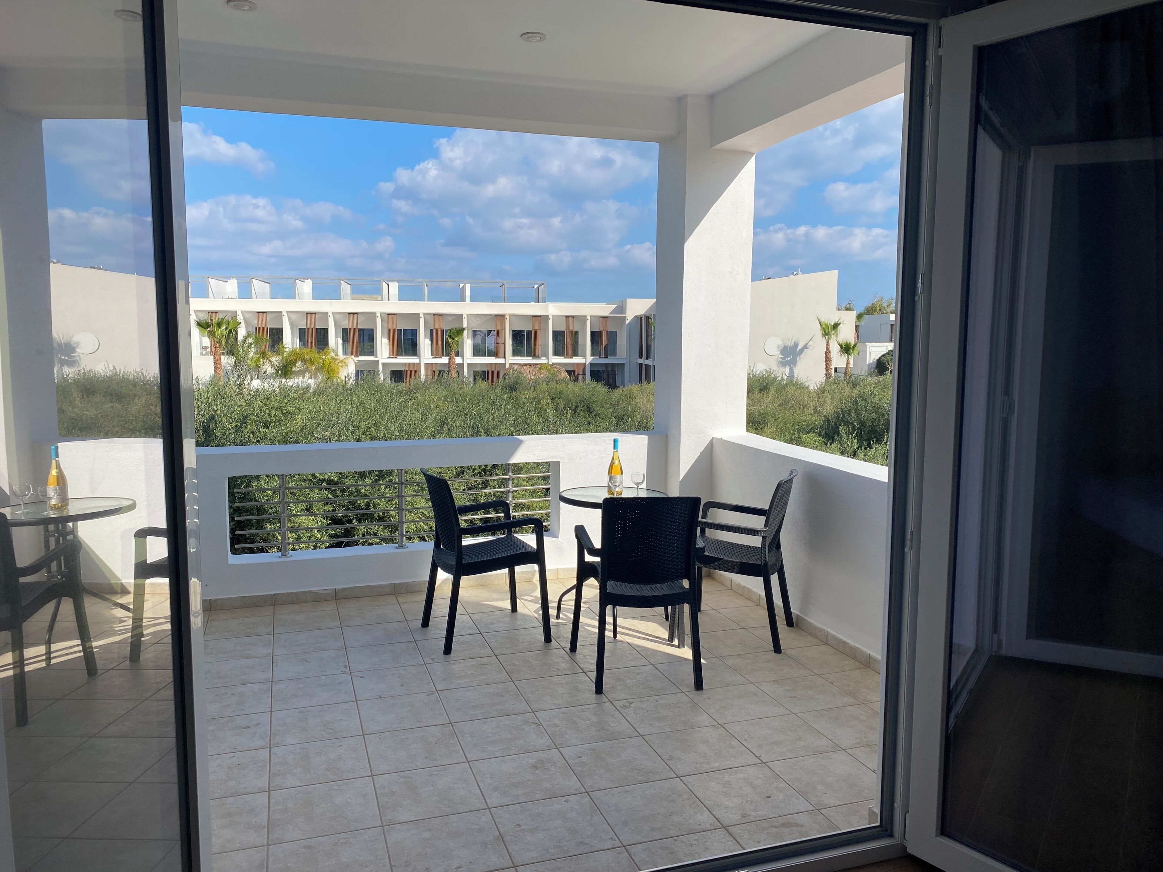 A balcony with a glass door, a small table with chairs, and a bottle of wine.