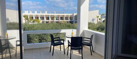 A balcony with a glass door, a small table with chairs, and a bottle of wine.