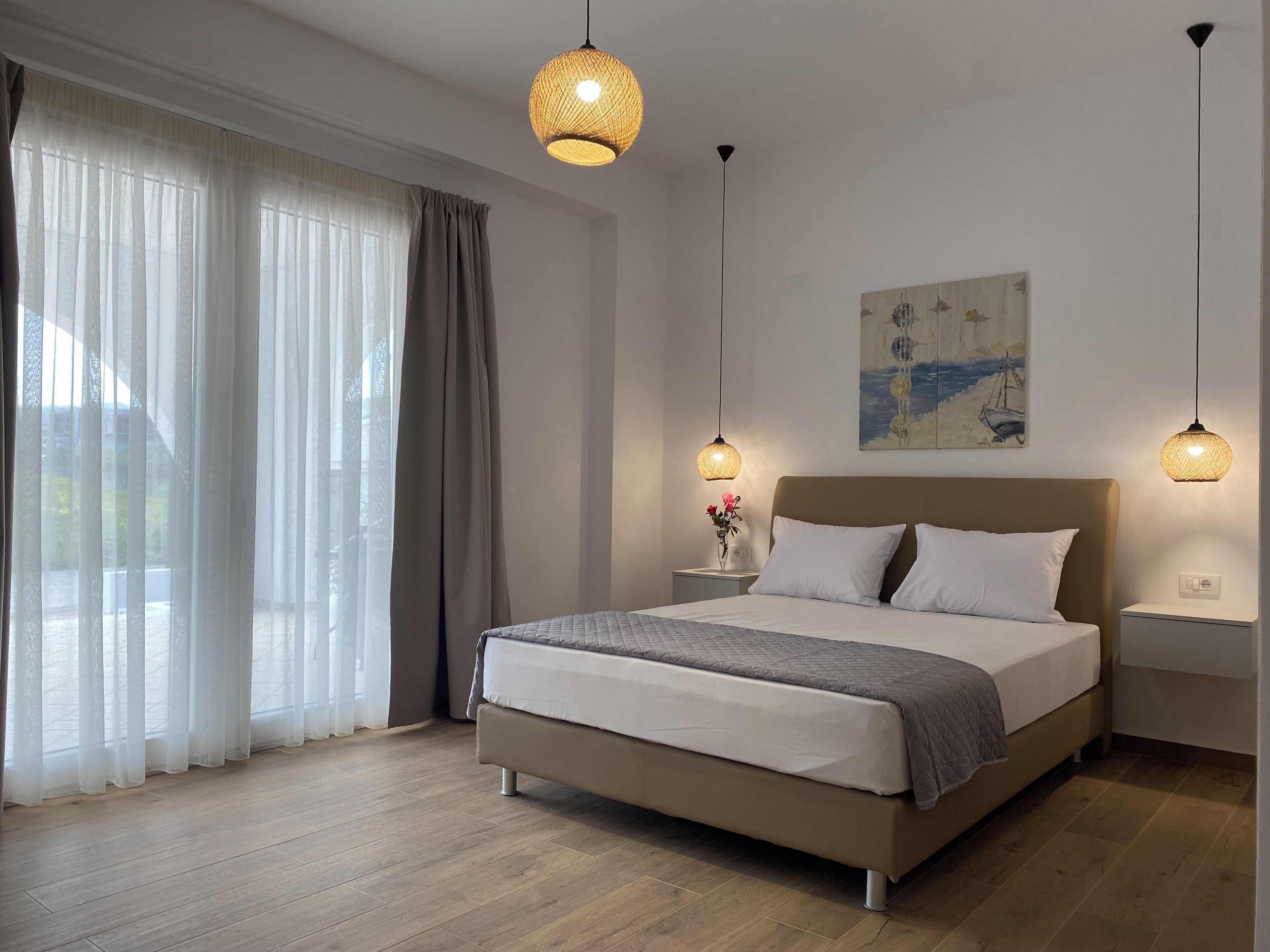A bedroom with a bed, two bedside tables, a painting on the wall, and a window with curtains.