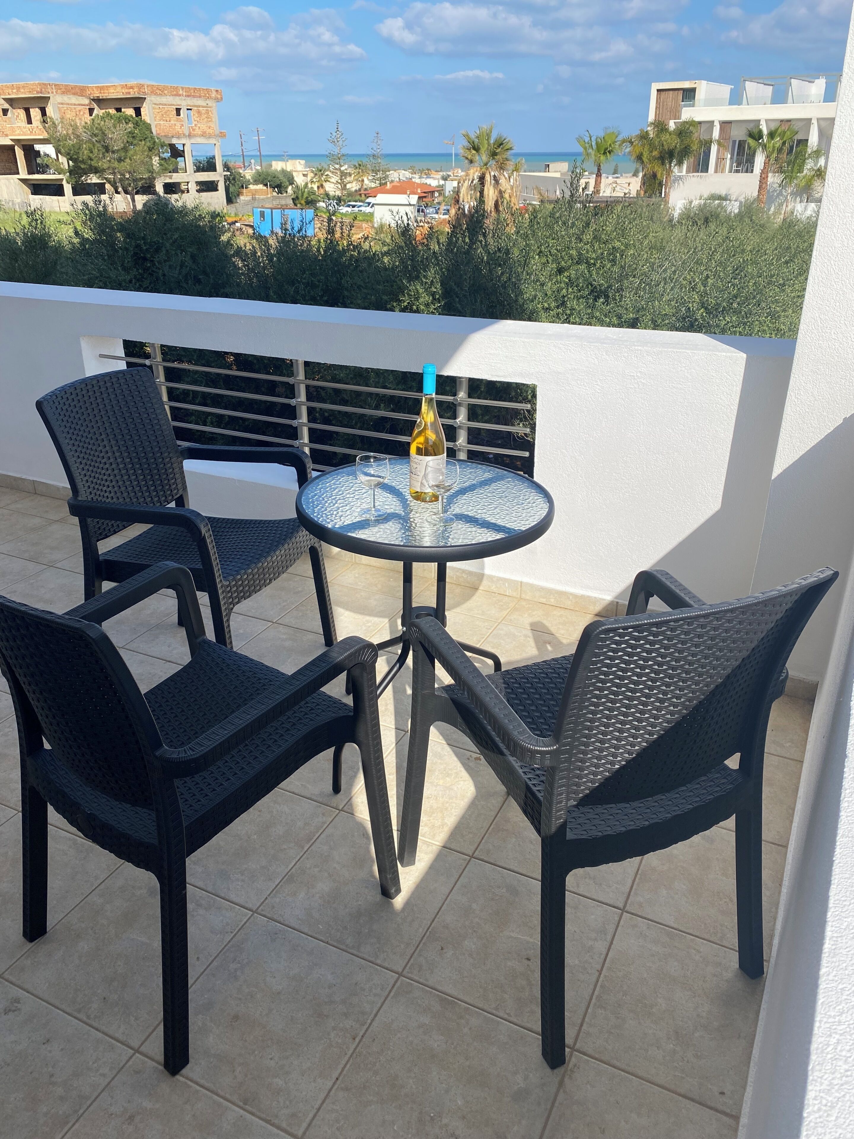 A terrace with a table and chairs, a bottle of wine, and a view of the sea and buildings.