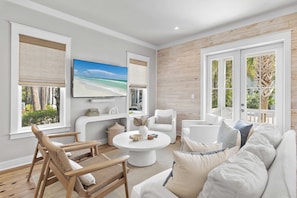 Una sala de estar con un televisor grande, muebles blancos y vista al mar a través de las ventanas.