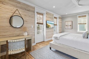 Un dormitorio con cama, escritorio, silla, espejo redondo y ventana con vistas.